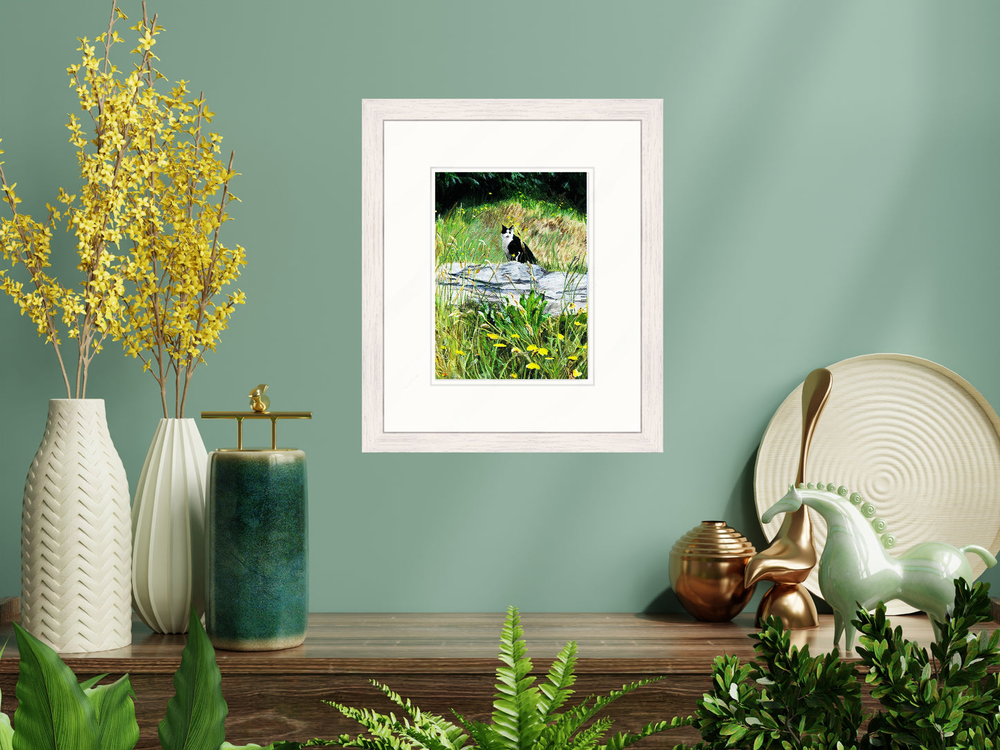 Framed picture of a cat in nature on a shelf with decorative items against a green wall.