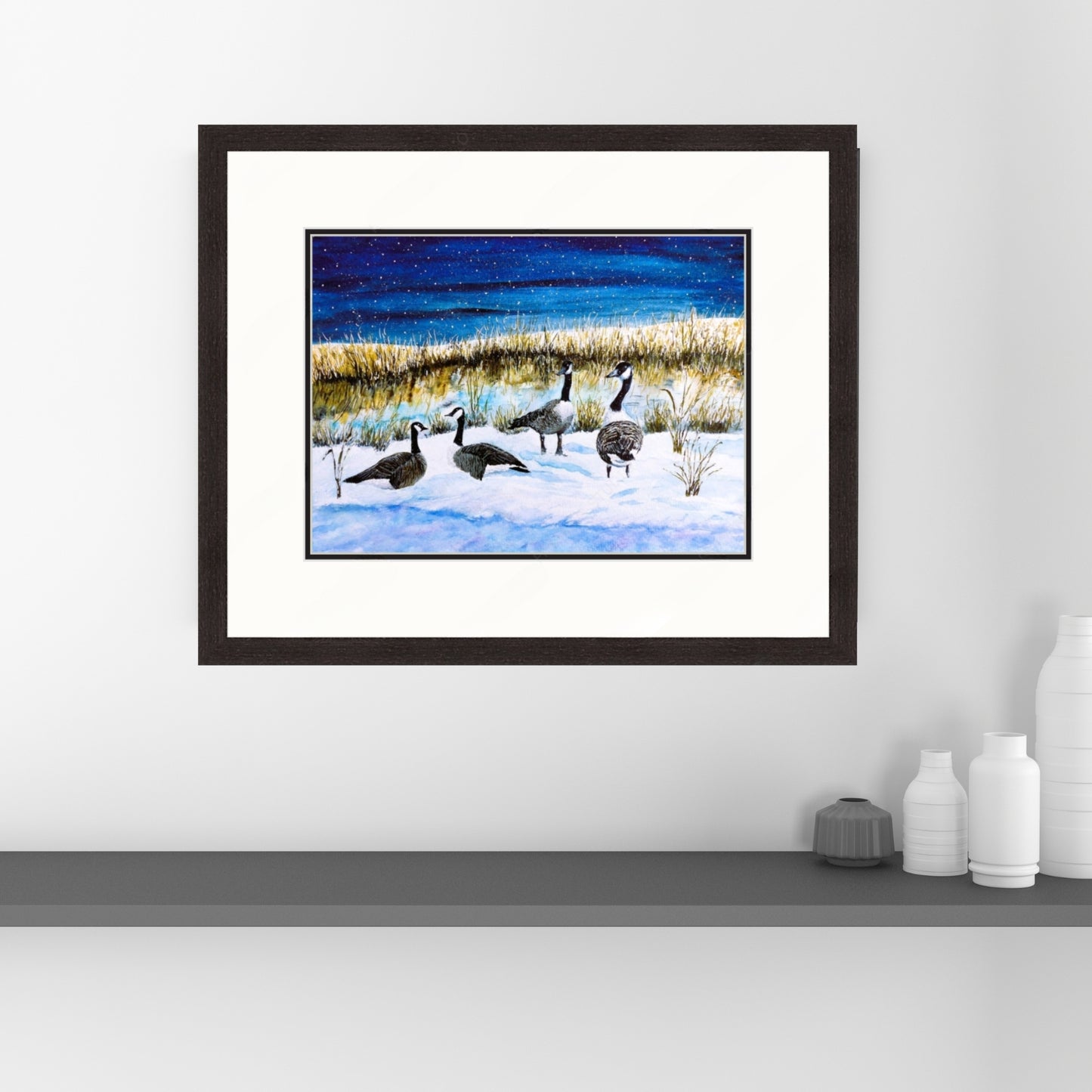 Framed artwork of geese on a snowy landscape hanging on a white wall.