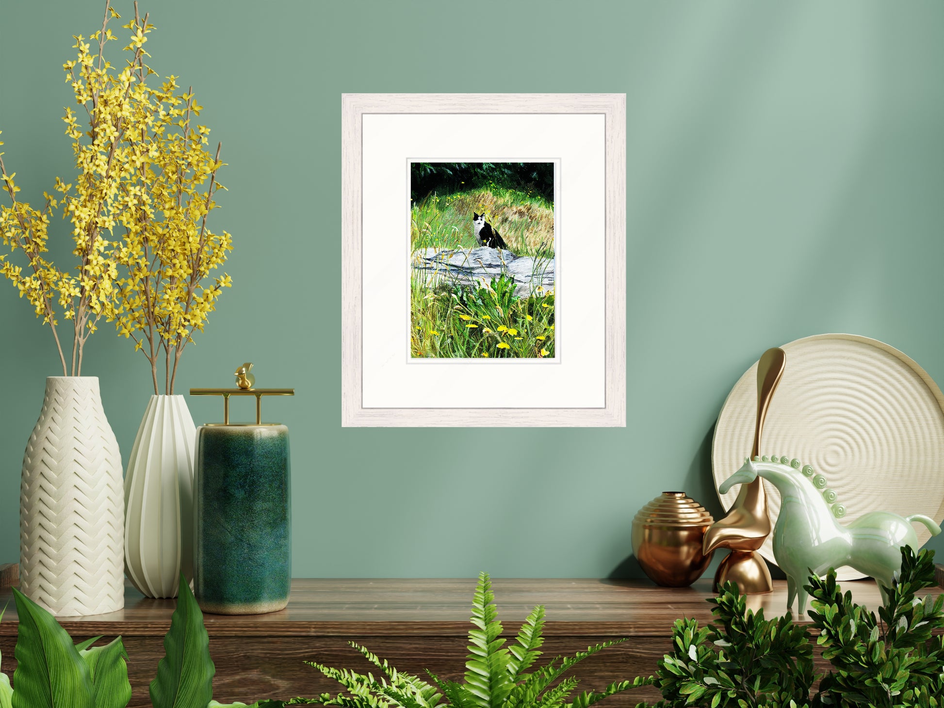 Framed picture of a cat in nature on a shelf with decorative items against a green wall.